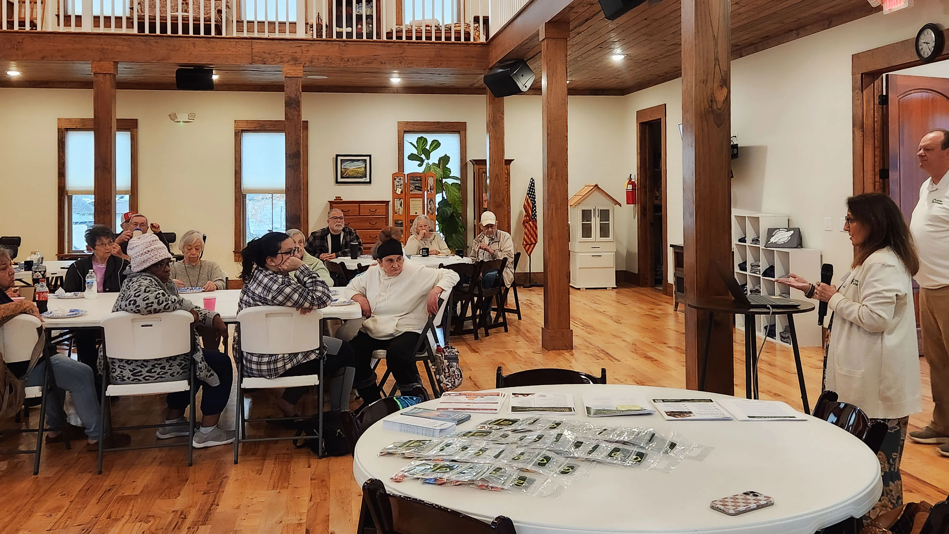 Neighbors sit at round tables with brochures spread out in front of them.