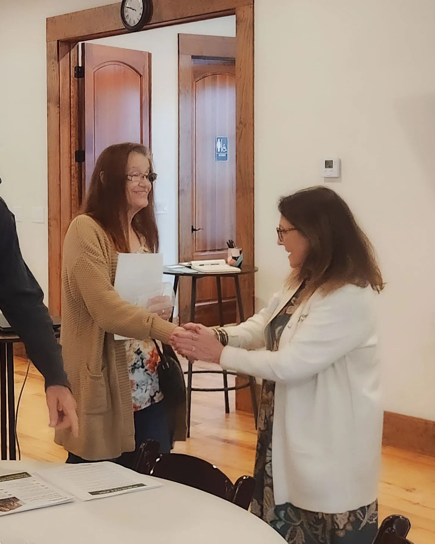 A Home Instead representative in a white cardigan shakes hands with a neighbor.