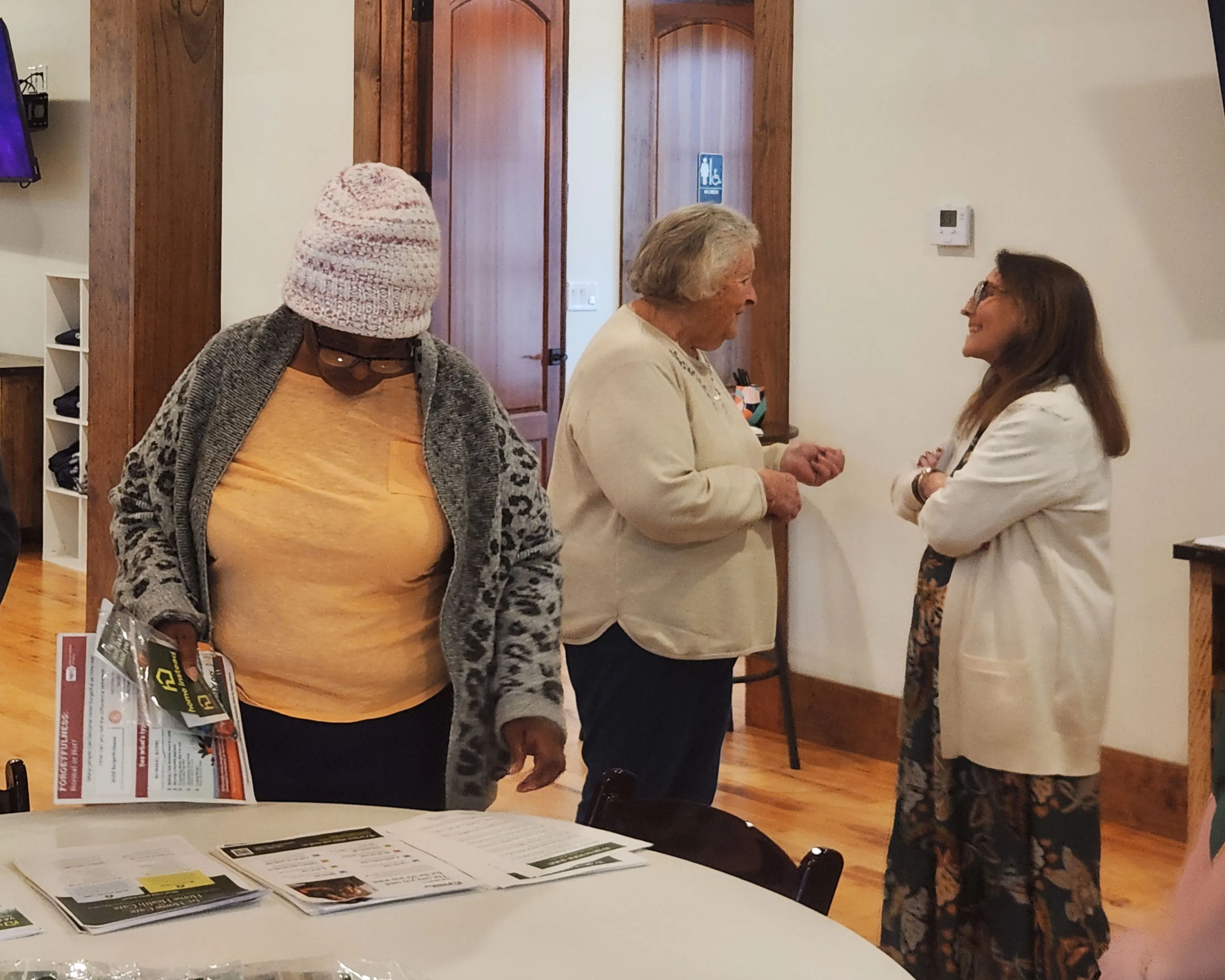 A Home Instead representative talks with two women holding brochures.