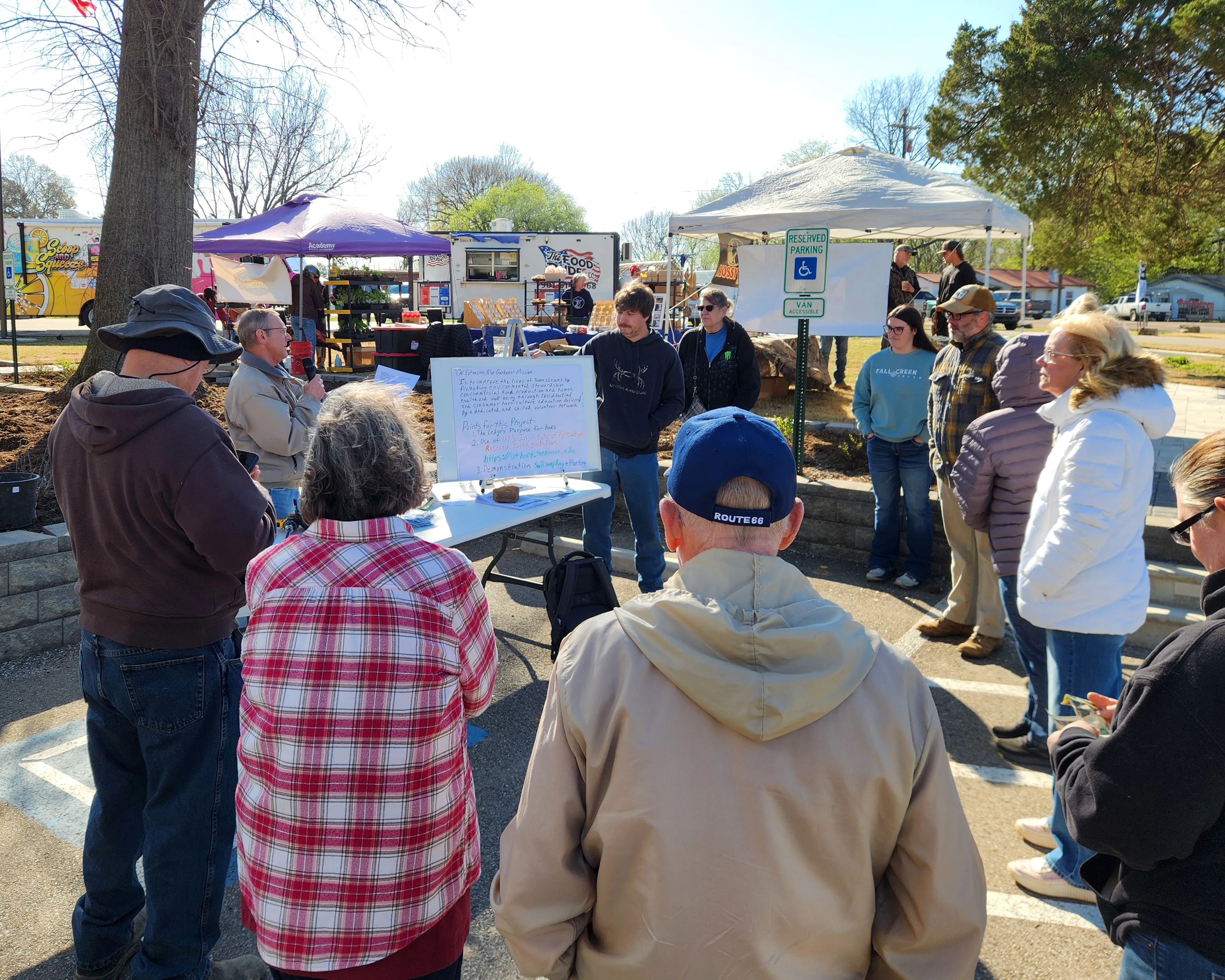 Neighbors gather outside near pop-up tents to hear a gardening demonstration at Seed Swap 2026.
