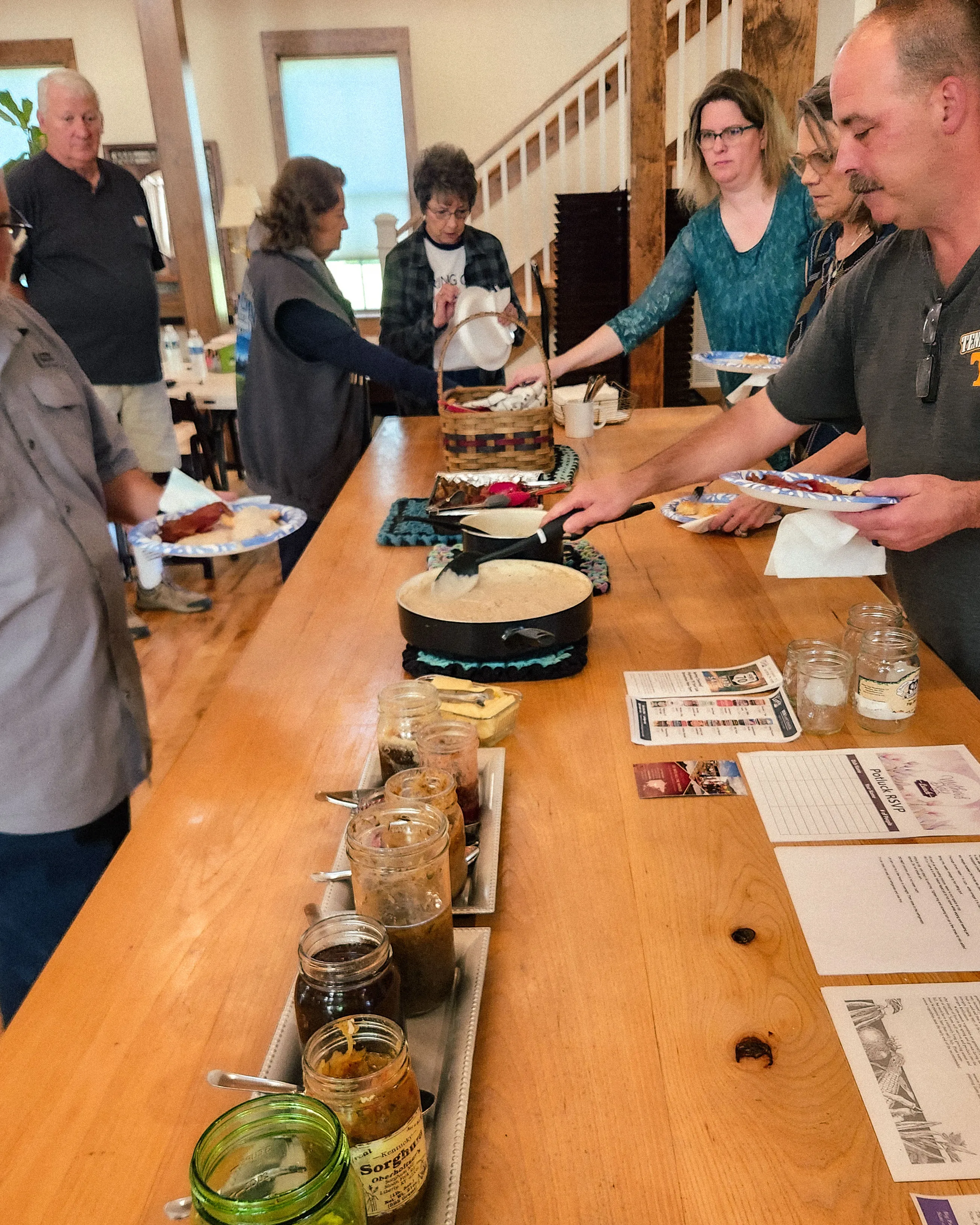 A breakfast buffet table with a skillet of food and jars, as guests fill their plates.