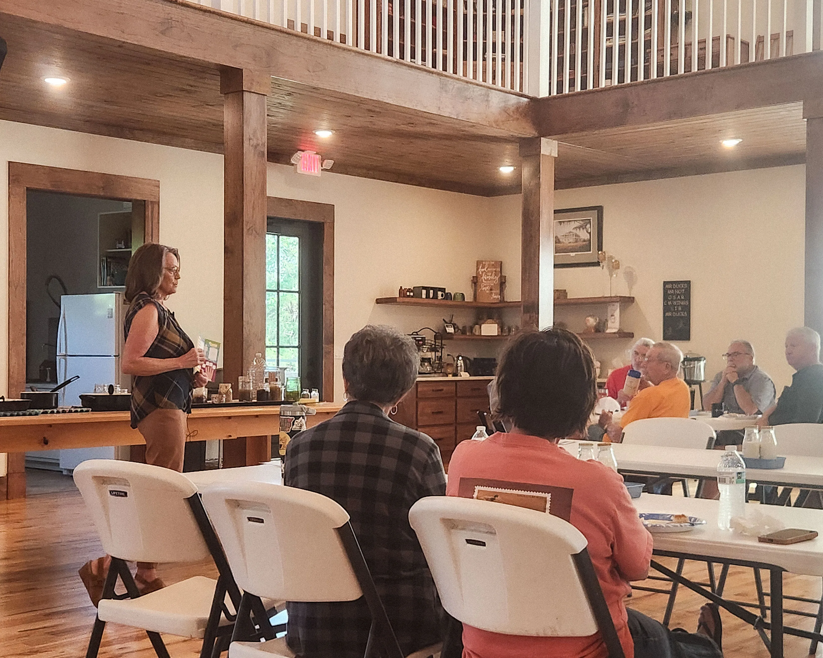 Kim Powell speaks to neighbors seated at tables in the main hall.