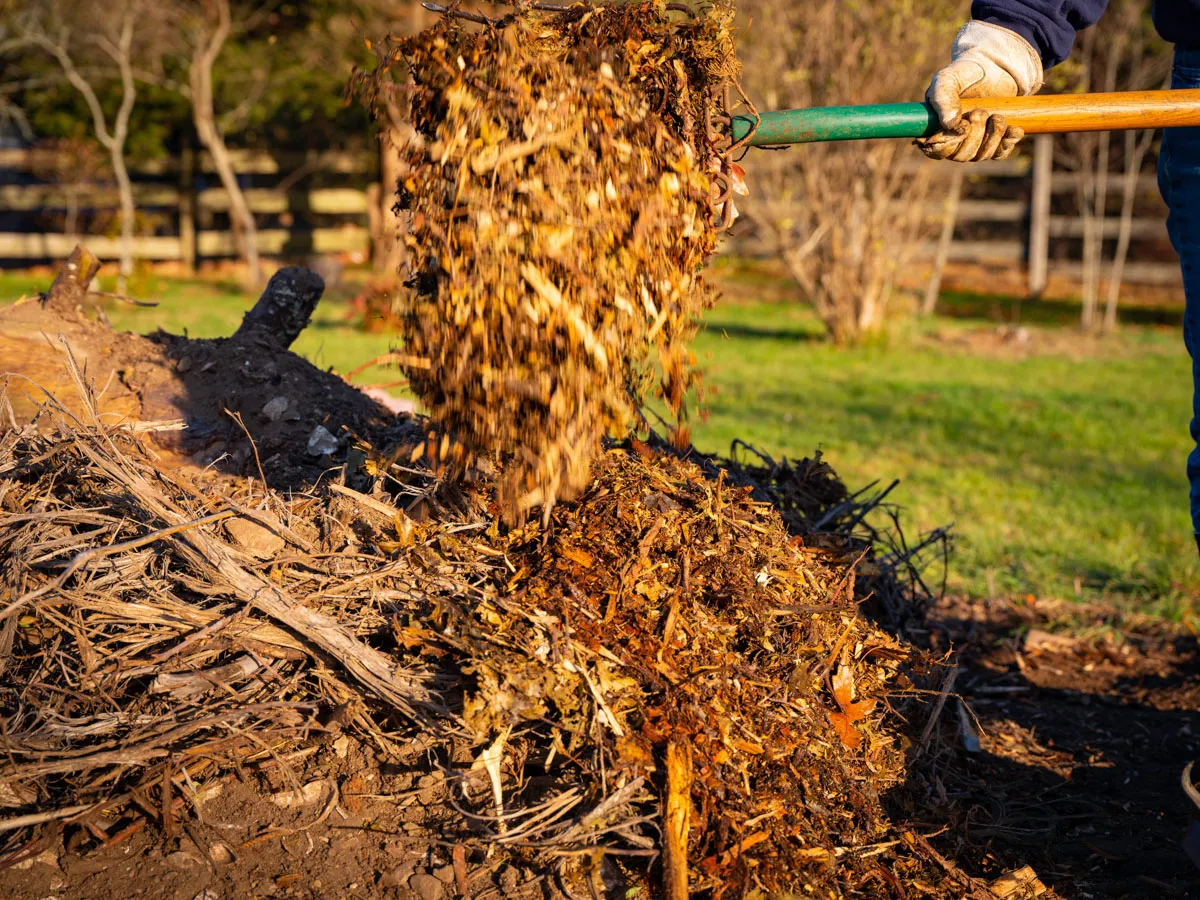 A shovel tosses steaming compost onto a pile in a field.