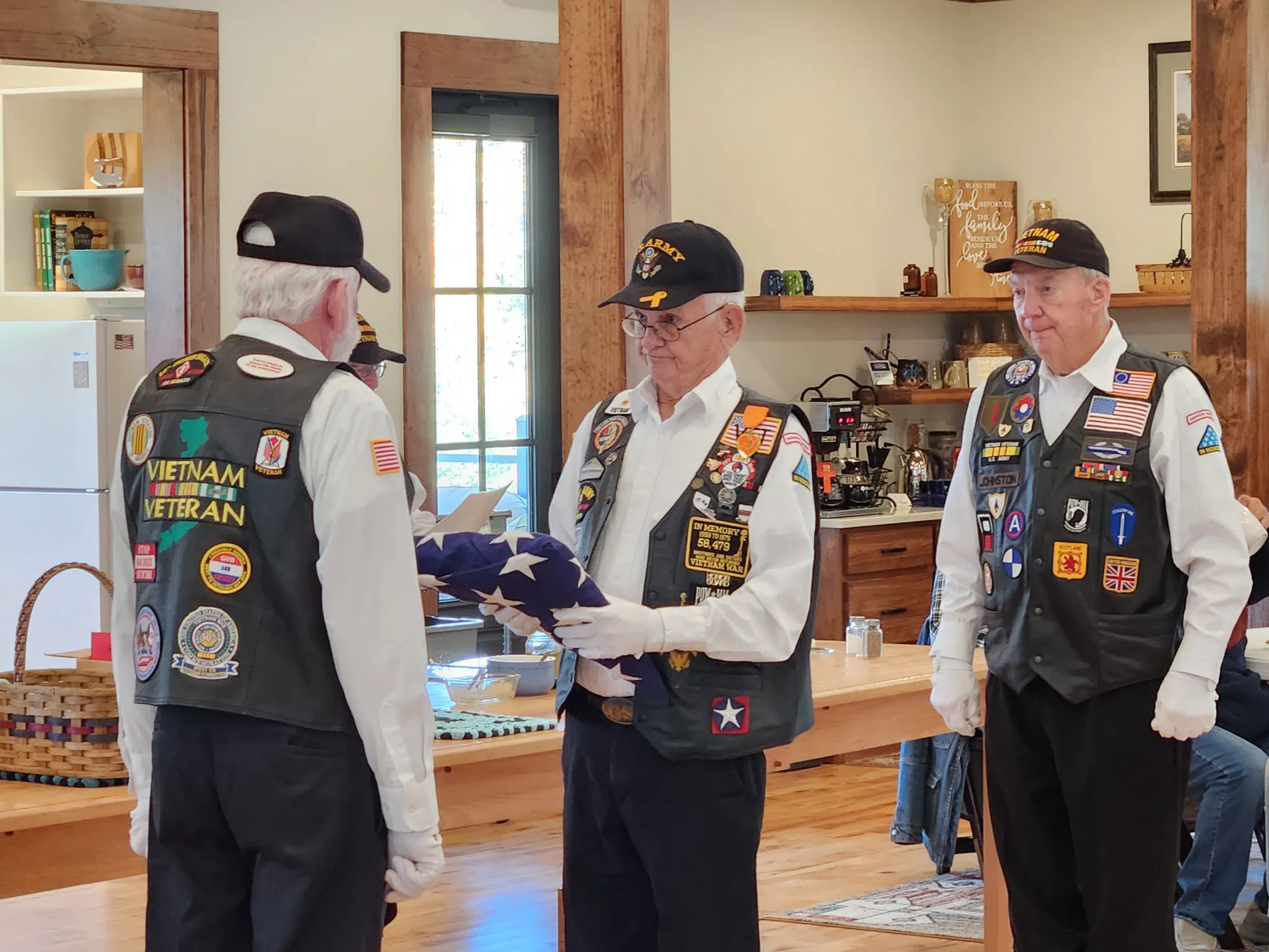 Three veterans in vests and caps hold a folded flag during the ceremony.