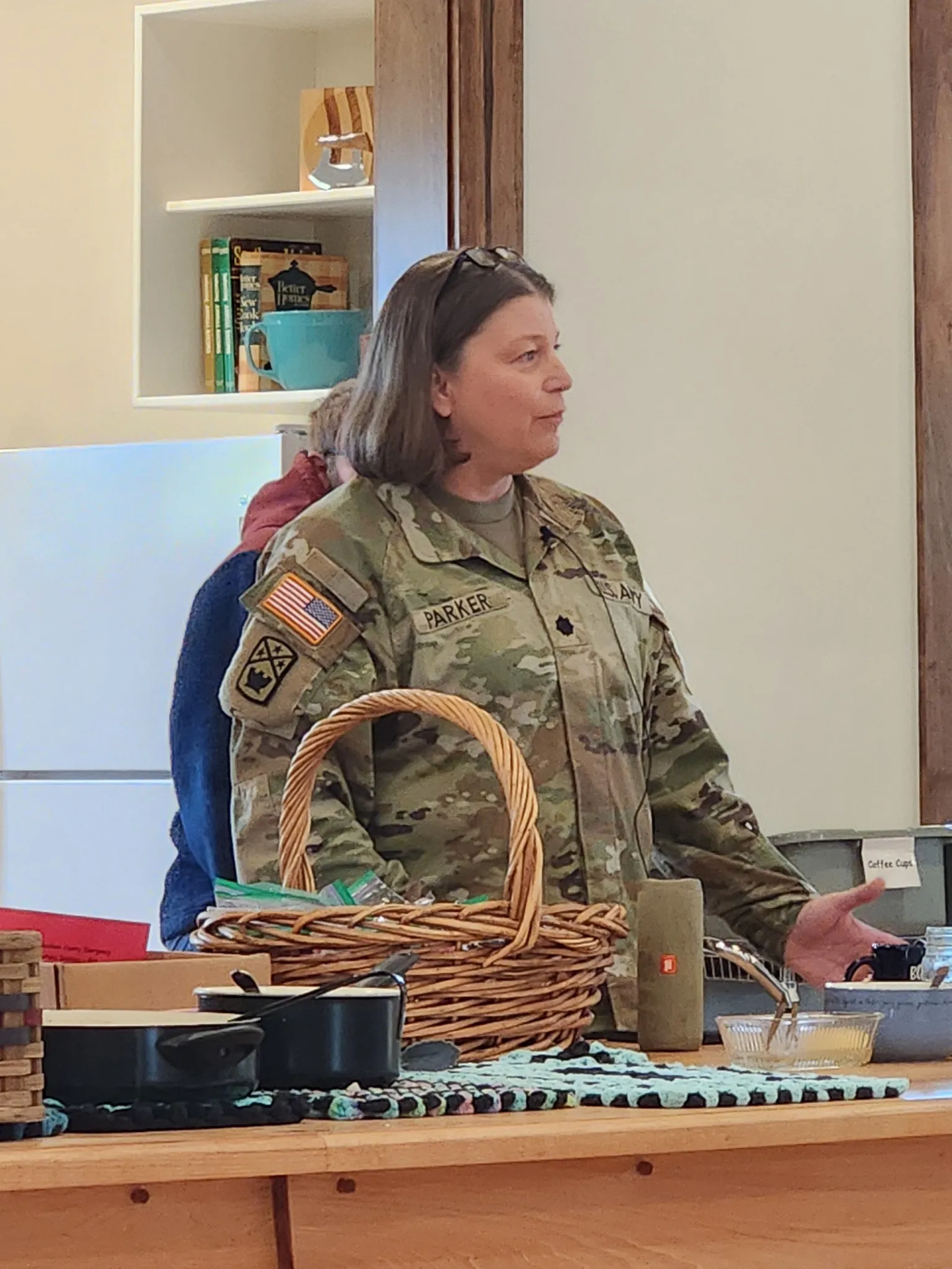 Lt. Col. Susan Parker, in an Army uniform, speaks to the group beside a wicker basket.