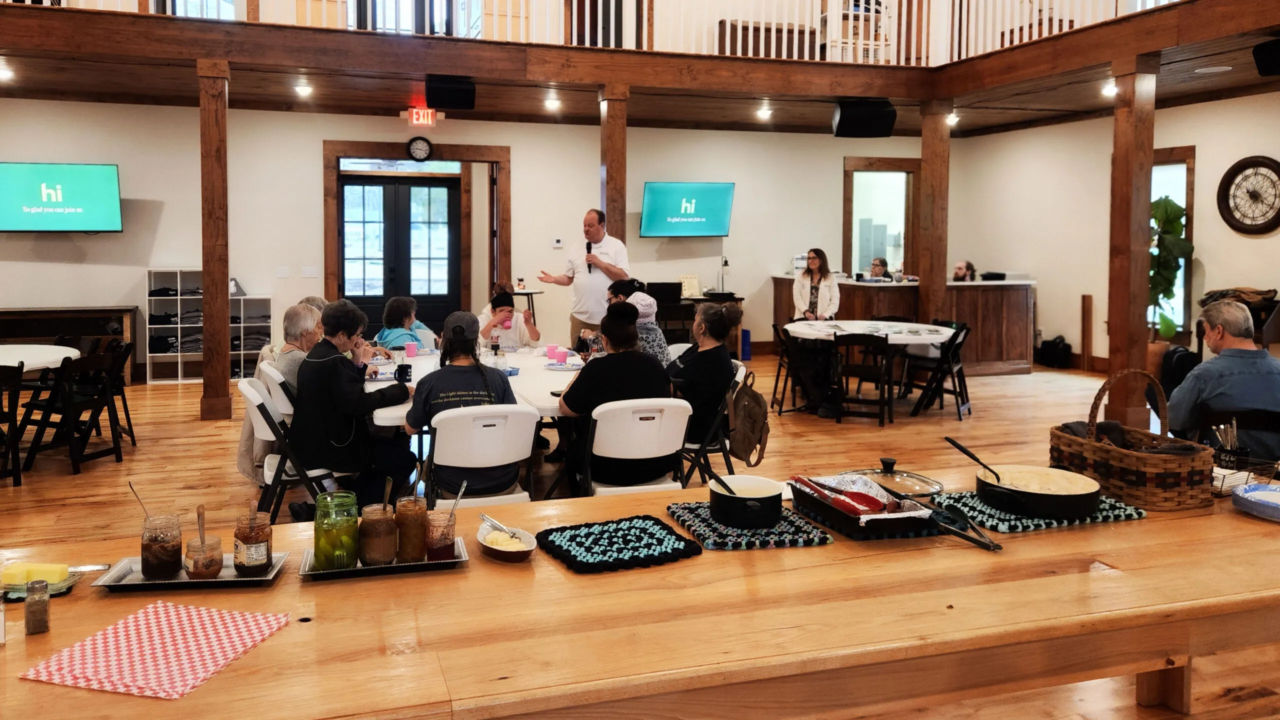 Neighbors sit at round tables in the hall while a Home Instead speaker presents, with a buffet in the foreground.
