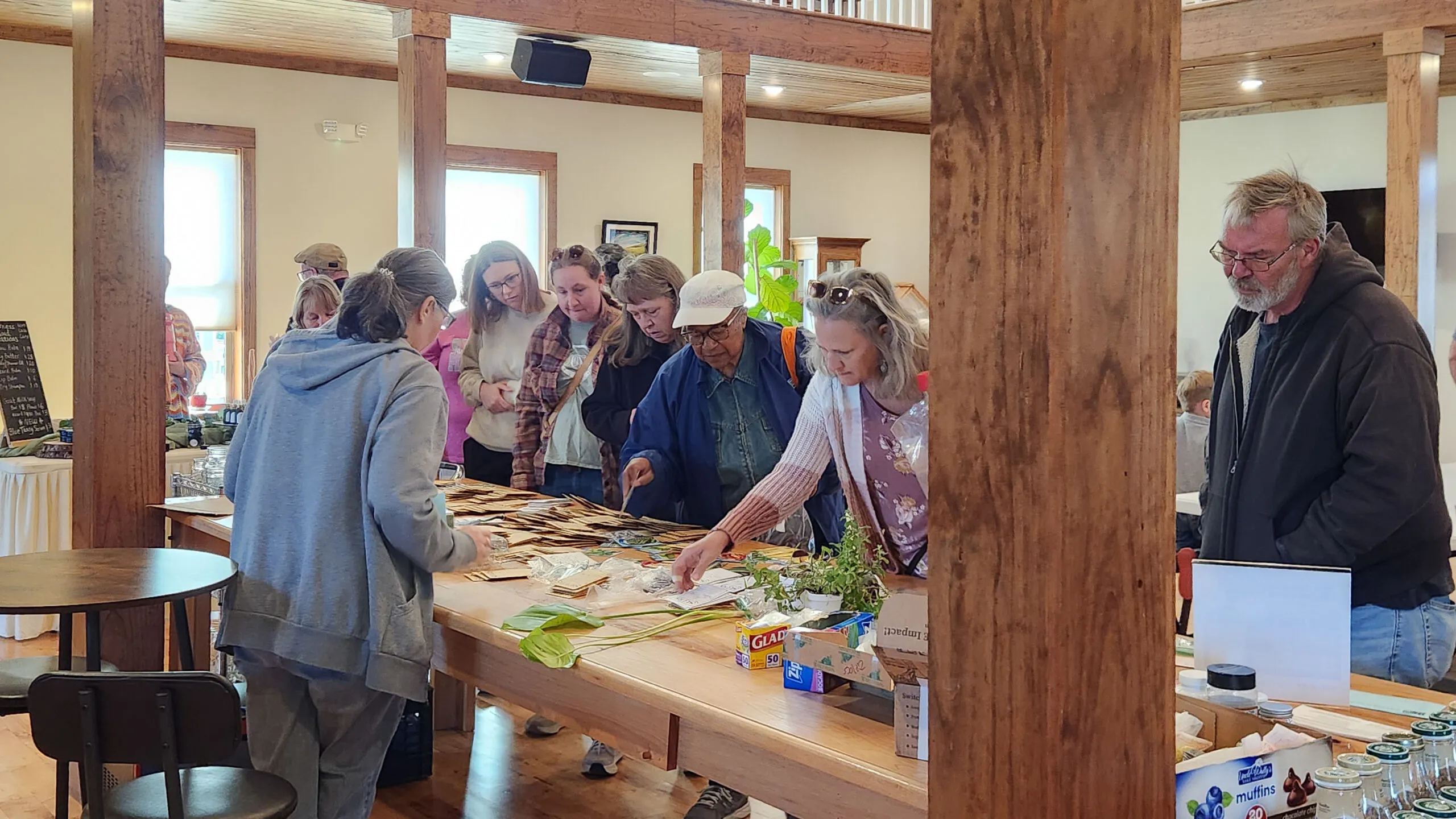 Neighbors gather around a long table of seeds and plants in the main hall at Seed Swap 2026.
